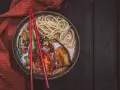 A miseczce z aromatycznym ramen wegetariańskim, pełnej makaronu, grillowanego bakłażana i pomidorów, spoczywają czerwone pałeczki.