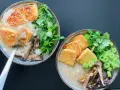 Dwie miseczki aromatycznego congee z chrupiącym tofu, grzybami i świeżymi ziołami.