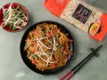 Makaron Chow Mein z warzywami i sezamem, gotowy do podania. Obok opakowanie makaronu i miseczka kiełków fasoli mung. Idealne do przepisów House of Asia.