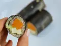 Rolka sushi z tofu, dynią i awokado, trzymana w dłoni.