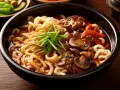 Gęsty, aromatyczny curry udon z wołowiną, grzybami i szczypiorkiem. Pyszne danie w czarnej misce.