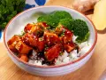 Miseczka ryżu z kawałkami lśniącego lososia teriyaki, posypanego sezamem i szczypiorkiem, obok parujących różyczek brokułów.