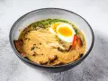 Miseczka aromatycznej zupy ramen z jajkiem na pół, plastrami mięsa, grzybami i szczypiorkiem.