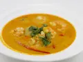 Aksamitna zupa tom yum z krewetkami, świeżą kolendrą i kawałkami chili na białym talerzu.