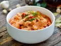 Pyszne wieprzowina w sosie curry, udekorowana szczypiorkiem i papryczką chili, podana w białej misce na drewnianym stole.