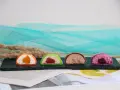 Cztery kolorowe mochi: pomarańczowe, zielone z malinami, czekoladowe i fioletowe z jagodami. Różne rodzaje słodkości.