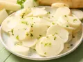 Plasterki białej rzodkwi, czyli daikon, posypane zielonymi ziołami na talerzu.