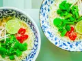 Dwie miseczki aromatycznej zupy pho z makaronem, mięsem, kiełkami, limonką, chili i świeżymi ziołami.