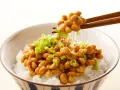 Miseczka ryżu z natto, japońską potrawą z fermentowanej soi, posypana szczypiorkiem. Pałeczki unoszą nitki natto.