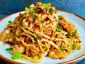 Pyszny makaron z wieprzowiną, posypany szczypiorkiem i sezamem, z dodatkiem płatków chili.
