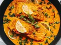 Aksamitny curry z łososiem w pomarańczowym sosie, udekorowane plasterkami cytryny i świeżymi ziołami.