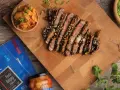 Pokrojony stek bulgogi polany sosem, obok miseczka z kimchi i opakowanie pasty do bulgogi.