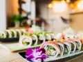 Wykwintne sushi z mięsem, ozdobione kwiatem i warzywami, prezentuje się apetycznie na talerzu.