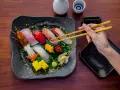 Wykwintne jedzenie w Japonii: ręka z pałeczkami sięga po świeże sushi i sashimi, obok sos i sake.