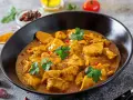 Aksamitny kurczak w sosie curry, jedno z popularnych potraw kuchni azjatyckiej, ozdobiony natką pietruszki i różowym pieprzem.