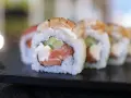 Uramaki co to? Rolka sushi z łososiem, awokado i krewetką, ryż na zewnątrz, na czarnej desce.