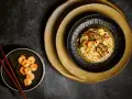 Chintan ramen z krewetkami i warzywami, podany na czarnym talerzu, obok miseczki z dodatkowymi krewetkami i pałeczkami.