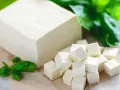 Kostka i pokrojone w kostkę tofu, obok zielone listki. Tak wygląda tofu – białe, delikatne, gotowe do przygotowania.