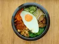 Apetyczne koreańskie jedzenie: miska bibimbap z jajkiem sadzonym, warzywami i mięsem na drewnianym tle.