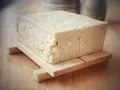 Duży blok domowego tofu na drewnianej podstawce, gotowy do przygotowania pysznych dań.
