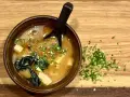 Miseczka aromatycznego miso shiru z tofu i wodorostami, posypana szczypiorkiem.