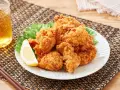 Chrupiące karaage chicken na talerzu, ozdobione plasterkiem cytryny i liśćmi sałaty. Obok szklanka złocistego napoju i pałeczki.