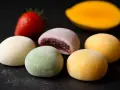 Kolorowe mochi, jak jeść? Delikatne kuleczki z nadzieniem, obok truskawka i mango.