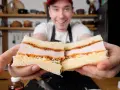 Uśmiechnięty mężczyzna prezentuje pyszne katsu sando z soczystym kotletem schabowym w panierce, delikatną kapustą i puszystym chlebem.