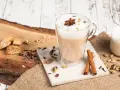 Aromatyczny napój, czyli chai, w szklance z pianką i anyżem. Obok cynamon, kardamon, goździki i ciasteczka.