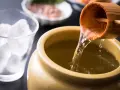 Nalewanie japońskiego alkoholu z drewnianej chochli do ceramicznego naczynia. Obok szklanka z lodem.