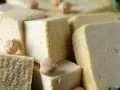 Kawałki miękkiego tofu ułożone obok siebie, niektóre z nich mają kratkowaną fakturę. Kilka ciecierzycy dodaje uroku.
