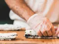 Ręce w rękawiczkach zwijają sushi na desce. Dowiedz się, jak zrobić zaprawę do ryżu sushi, by uzyskać idealny smak.