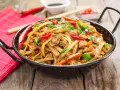 Pyszny makaron chain main z kurczakiem, papryką i chili, posypany natką pietruszki, w czarnej woku.