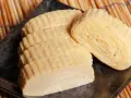 Trzy porcje nigiri tamago, delikatnie zwiniętego omletu jajecznego, ułożone na czarnym talerzu na tle bambusowej maty.