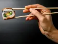 Dłoń trzyma pałeczkami jedno sushi. Zastanawiasz się, ile sushi na osobę będzie idealne na kolację?
