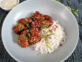 Pyszny kurczak po koreańsku w sosie, posypany sezamem i szczypiorkiem, podany z ryżem.