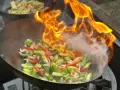 Ogień płonie w woku, przygotowując warzywa do stir fry. To szybkie smażenie, które zachowuje świeżość składników.