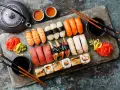Piękne składniki na sushi: nigiri z łososiem, krewetkami, tuńczykiem, węgorzem i rybą maślaną, a także rolki. Obok czajniczek, sos sojowy i marynowany imbir.