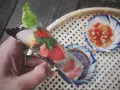 Ręka trzyma świeże rolls z papieru ryżowego z truskawkami i ziołami. Obok miseczki z sosem.