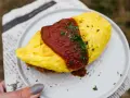 Pyszny omlet ryżowy polany sosem pomidorowym i posypany natką pietruszki, podany na talerzu.