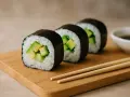 Linia świeżego sushi z awokado na drewnianej desce, obok sosu sojowego i pałeczek.