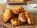 Chrupiące nuggetsy w panko z piekarnika, idealne do maczania w sosie. Obok szklanka mleka i miseczka jogurtu.