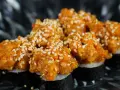 Pyszne sushi z tatarem z łososia, posypane sezamem, prezentuje się apetycznie na ciemnym talerzu.