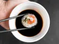 Pałeczkami zanurzam rolkę sushi w ciemnym sosie. Idealny sos słodki do sushi podkreśla smak ryby i ryżu.