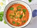 Aksamitny tom yum z kurczakiem, grzybami i kolendrą w misce z niebieskim wzorem. Obok leży łyżka.