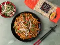Pyszny makaron sojowy z kurczakiem jak od chińczyka, z kiełkami fasoli mung i szczypiorkiem. Obok opakowanie makaronu chow mein.