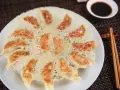 Chrupiące pierożki gyoza ułożone na talerzu, z chrupiącą panierką z ciasta. Obok miseczka sosu sojowego i pałeczki.