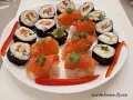 Piękne sushi kompozycje na białym talerzu: rolki z łososiem, awokado i papryką, ozdobione kolendrą.