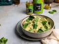 Aksamitny kurczak w zielonym curry, udekorowany świeżym szpinakiem i kolendrą. Obok puszka mleka kokosowego i słoiczek pasty curry.