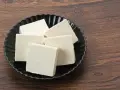 Kilka kostek białego tofu na czarnym talerzu. Czy tofu można mrozić? Tak, po rozmrożeniu zmienia teksturę, stając się bardziej gąbczaste.